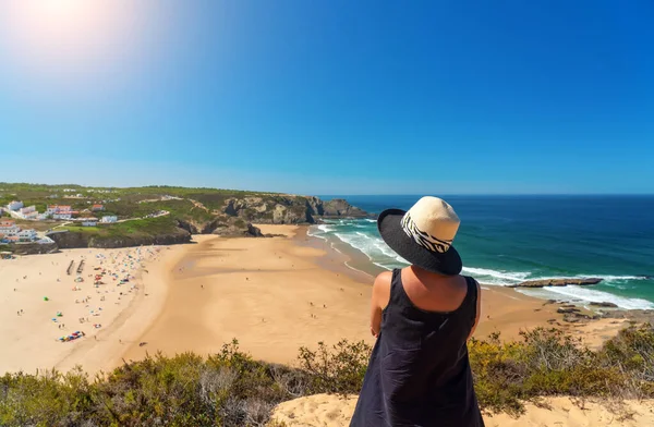 Una mujer con un sombrero en la cabeza, en la orilla, admira la vista de la playa portuguesa, Odeceixe. —  Fotos de Stock