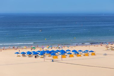 Daha çok mavi şemsiyeler, temiz su ve gökyüzü olan temiz bir kumsal..