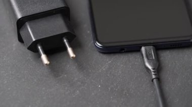 Gri yüzeyde kapatılmış akıllı telefonun şarj cihazının yakın plan görüntüsü döndürülüyor.
