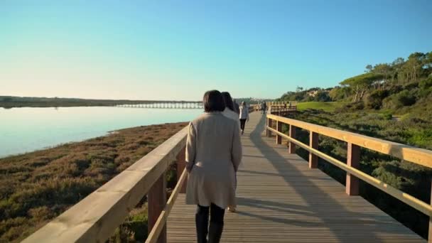 Due femmine che camminano su una passerella vicino a una riva del fiume con gente davanti. Sao Lourenco Quinta de Lago, Almancil. Portogallo — Video Stock