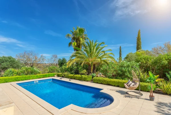 Piscina luxuosa no jardim de uma moradia privada, cadeira pendurada com almofadas para turistas de lazer, no verão. Portugal, Algarve. — Fotografia de Stock