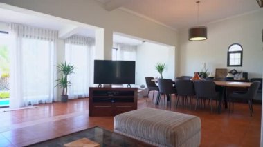 Oturma odasındaki klip TV 'yi, bir masayı ve pencerenin dışındaki havuza doğru çekimleri gösteriyor..