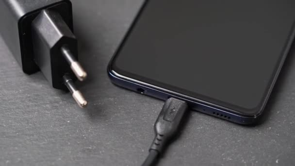 Primo piano rotante del caricabatterie collegato allo smartphone spento sulla superficie grigia. — Video Stock