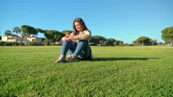 Sidovy av ung flicka med hjälp av smartphone på en gräsbevuxen fält med solen skiner i bakgrunden. — Stockvideo