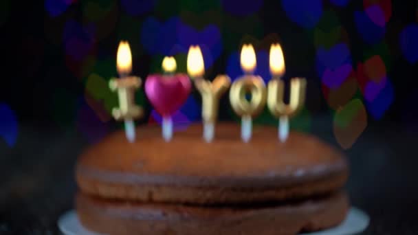 Tirada desenfocada de pastel colocada sobre una mesa que poco a poco se centra en las velas ortografía te amo, para el Día de San Valentín. — Vídeos de Stock