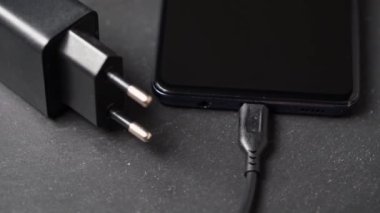 Gri yüzeyde kapatılmış akıllı telefonun şarj cihazının yakın plan görüntüsü döndürülüyor.