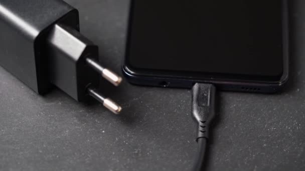 Rotierende Nahaufnahme des in ausgeschaltetes Smartphone eingesteckten Ladegeräts auf grauer Oberfläche. — Stockvideo