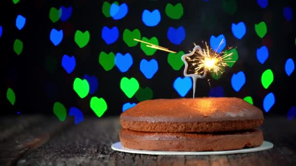 Torta minimalista colocada en una mesa con una chispa en forma de estrella que se enciende, en celebración de Año Nuevo. En el fondo, luces borrosas, bokeh de corazones parpadean. — Vídeo de stock