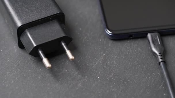 Memutar close-up pengisi daya yang ditancapkan mematikan smartphone pada permukaan abu-abu. — Stok Video