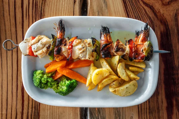 Brochette de fruits de mer grillée faite de crevettes, de poissons et de poivrons avec des chips, des carottes et du brocoli sur le côté. — Photo