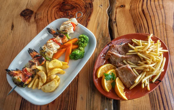 Gegrilde visspiesje met links chips en groenten. Bord van biefstuk met frietjes, versierd met sinaasappel aan de rechterkant. — Stockfoto