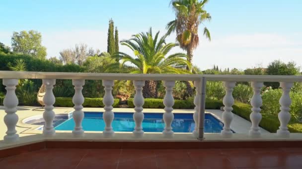 Luxurious view from the window to the pool with a rocking chair and a garden of palm trees. — Stock Video