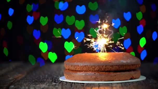 Torta minimalista colocada en una mesa con una chispa en forma de estrella que se enciende, en celebración de Año Nuevo. En el fondo, luces borrosas, bokeh de corazones parpadean. — Vídeo de stock