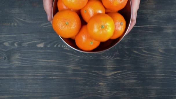 Ovanifrån, män händer placeras, en metallskål med mogna mandariner, en källa till vitamin C. På en trä bakgrund. — Stockvideo