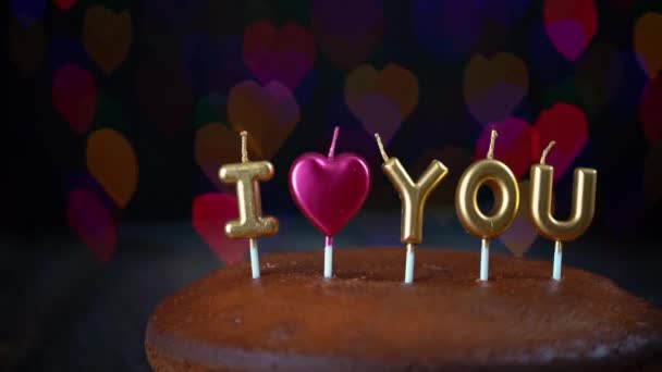 Pan shot of simple Valentines Day cake with lit i love you candles, with a colorful background. In the background, blurry lights, bokeh of hearts blink. — Stock Video