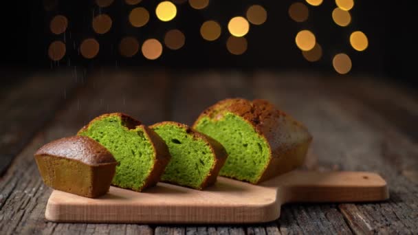 Stollen Christmas bread made of spirulina and pistachios, sprinkled with powder for the holidays. On a wooden table, bokeh lights on the background. — Stock Video