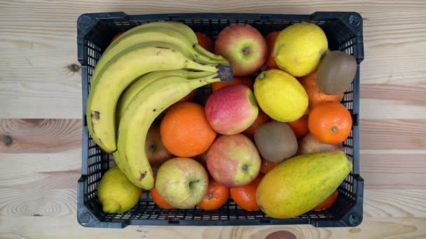 Een man gooit mandarijnen op een doos tropisch exotisch fruit, in slow motion. Op een houten achtergrond, bovenaanzicht. — Stockvideo