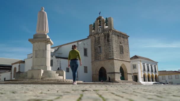 Chica turística pasea por la plaza de la antigua iglesia de Santa María cerca del monumento Obispo Francisco Gomes de Avelar. Faro Algarve — Vídeos de Stock