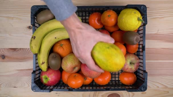 En man lägger exotiska frukter i en låda för att leverera mat under en pandemi. Hjälpa de fattiga. Platt äggläggning. — Stockvideo