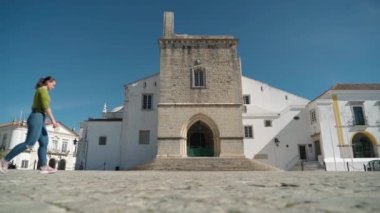 Kız turist Faro şehrindeki Santa Maria antik kilisesinin meydanında yürüyor. Villa Adentro, Algarve.