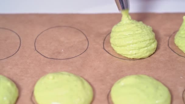 Baker met behulp van een banketbakje zak om ronde vormen in te vullen op perkament papier met een andere gekleurde tint van roze beslag. Vervaardiging van macarons. — Stockvideo