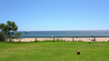 Yeşil bir çayır manzarası ve arka planda kumlu bir plaj ve okyanusta bir yatı var. Vale do Lobo, Portekiz.