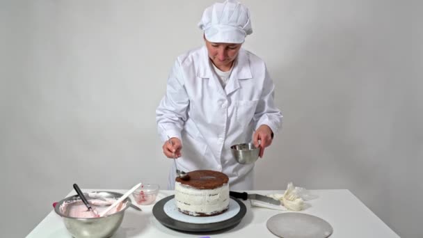 한 중년 여성 제빵사가 초콜릿 브라우니와 함께 웨딩 케이크에 시럽을 붓습니다.. — 비디오