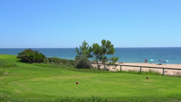 Vista de um campo de relva verde e uma praia de areia no fundo com um yatch no oceano. Vale do Lobo, Portugal. — Vídeo de Stock