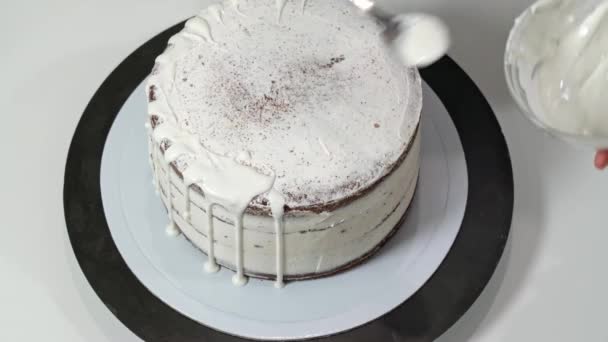 Вид зверху пекарні, що наливає розтоплений білий шоколад по краях торта, так що він падає вниз по боках . — стокове відео