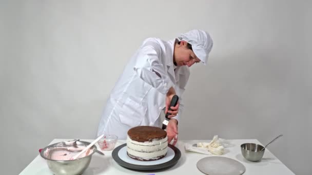 Prise de vue avant d'un boulanger à l'aide d'une spatule glaçante pour retoucher soigneusement les côtés du gâteau recouvert de crème. — Video