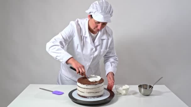 Voorste schot van een bakker met behulp van een glazuur spatel om zorgvuldig aan te raken zijkanten van room bedekt taart. — Stockvideo