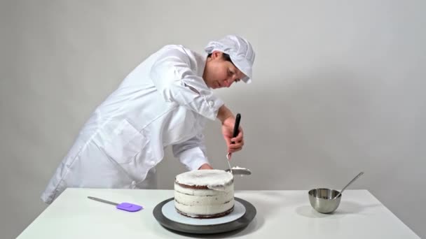 Přední záběr pekaře pomocí třešňové špachtle opatrně dotknout strany smetanové kryté dort. — Stock video