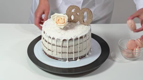 Beautiful birthday cake, decorated with macarons and a rose, being proudly presented by a female baker. — Stock Video