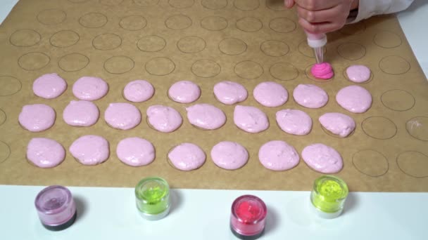 Boulanger en utilisant un sac à pâtisserie pour remplir des formes circulaires sur du papier parchemin avec une teinte différente de pâte rose. Fabrication de macarons. — Video