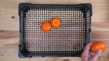 Bir adamın elleri, salgın sırasında bir teslimat kutusunda olgun bir mandalina, egzotik bir meyve yatıyordu. Ahşap bir arka planda.