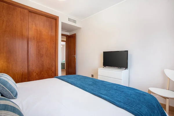 Shot from corner of bedroom, view from bed to a tv on a stand, a wardrobe on the side and an open door showing another room.