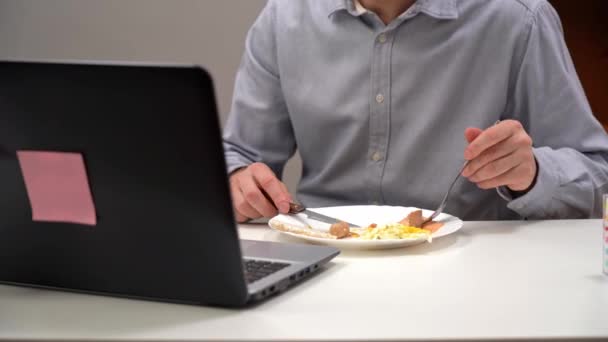 Un joven oficinista, un gerente, come su dieta en su oficina en casa, durante el aislamiento, una pandemia. Con una computadora en primer plano. — Vídeo de stock