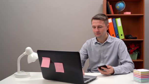 Trabajador de oficina joven, gerente, está escribiendo texto en el teléfono y en la computadora. Primer plano. — Vídeo de stock