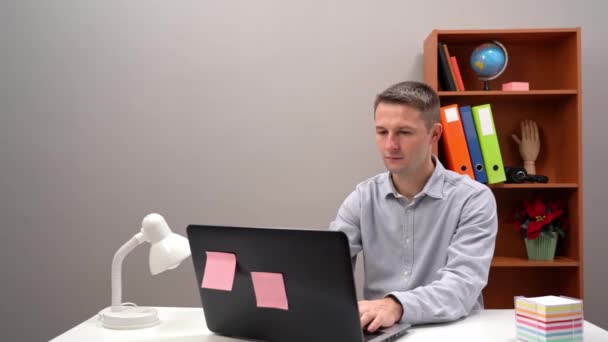 Ung kille kontorsarbetare, chef, skriver i datorn och på ett papper klistermärke. Närbild. — Stockvideo