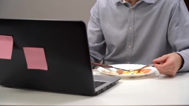 Een jonge kantoormedewerker, een manager, eet zijn dieet in zijn eigen kantoor, tijdens isolatie - een pandemie. Met een computer op de voorgrond. — Stockvideo