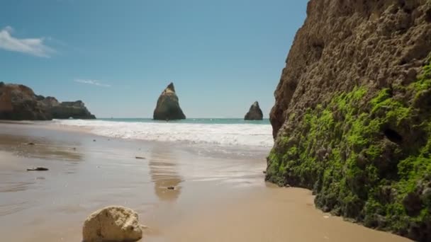 Movimento para a frente, estabilizado, no mar, na praia da Prainha, perto do muro de pedra são cobertos com musgo verde. — Vídeo de Stock