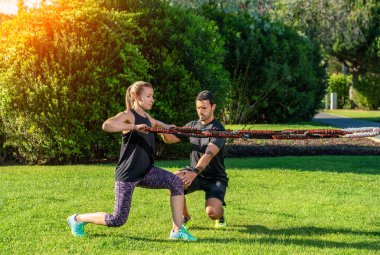 Spor salonundaki antrenör ve müşteri lastik genişletici ve gerilim bandıyla egzersiz yapıyor. Parkta, dışarıda..