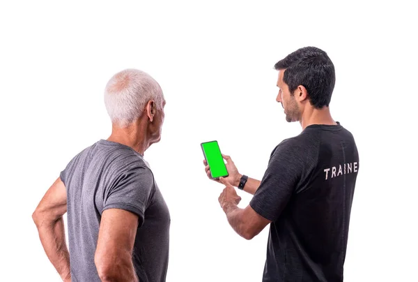 Un istruttore di fitness spiega a un anziano cliente come utilizzare un'applicazione software per l'allenamento su uno sfondo bianco isolato. — Foto Stock