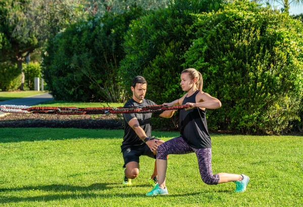 Fitness trenér a klient v parku cvičení s gumovým expandérem, napínací pásy. Na venkovní v parku. — Stock fotografie