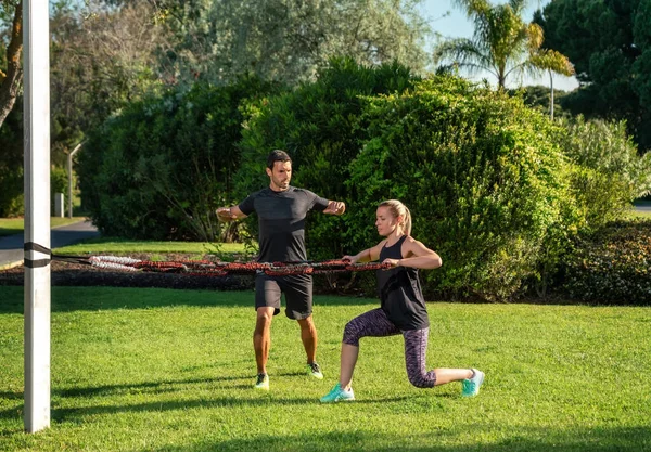 Fitness edző és ügyfél a parkban gyakorlat gyakorlatok egy gumi expander, feszültség sávok. A szabadban a parkban. Jogdíjmentes Stock Képek