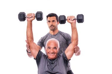 Spor hocasıyla egzersiz yapan yaşlı bir erkek müşteri, dambılları kaldırıyor. İzole edilmiş beyaz bir arkaplanda.