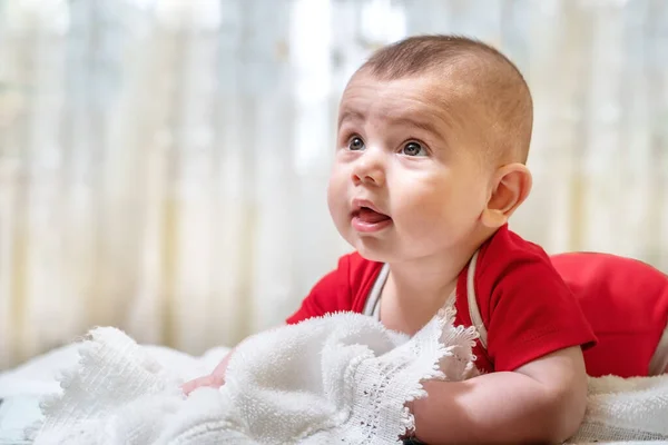 Ein neugeborenes gesundes Baby, ein Junge von vier Monaten, liegt glücklich auf dem Bauch. Vor dem Hintergrund des Schlafzimmers. — Stockfoto