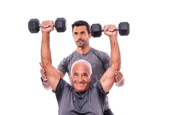 Elderly male client exercising with a fitness trainer, lifts dumbbells. On a white isolated background. — Stock Photo, Image