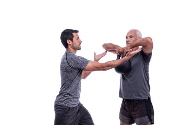 Spor hocasıyla egzersiz yapan yaşlı bir erkek müşteri, dambılı kaldırıyor. İzole edilmiş beyaz bir arkaplanda.