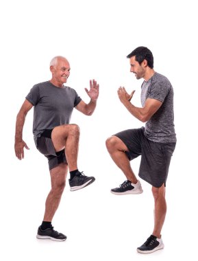 Yaşlı bir erkek müşteri spor antrenörüyle egzersiz yapıyor, yerinde yürüyor, adımlar atıyor. İzole edilmiş beyaz bir arkaplanda.